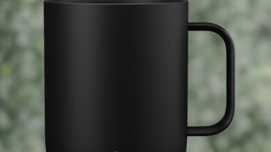 Schwarze Ember Smart Mug 2 mit Logo auf Holztisch vor verschwommenem grünen Hintergrund